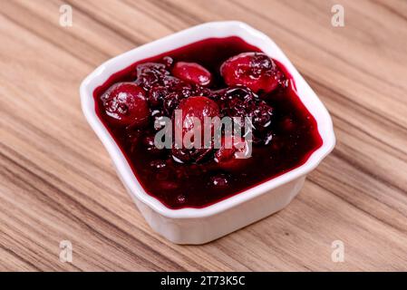 Marmellata di frutti di bosco in un recipiente bianco su una superficie di legno Foto Stock