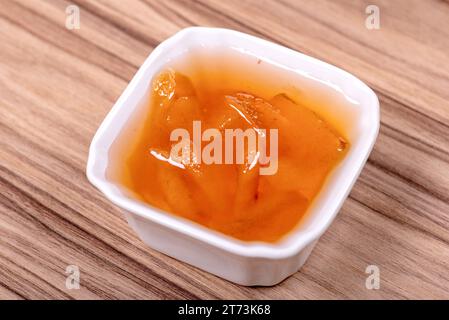 Marmellata di pesca dolce in un recipiente bianco di porcellana su una superficie di legno Foto Stock