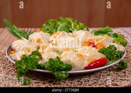 Manty (gnocchi di carne) è un piatto nazionale dei paesi dell'Asia centrale su un piatto con carote e verdure Foto Stock