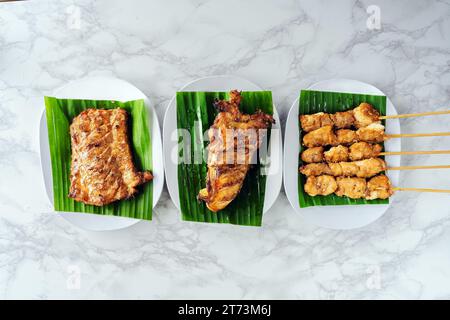 Vista dall'alto di diversi coccodrilli grigliati su foglie di banana sopra un piatto bianco su sfondo di marmo. Coccodrillo con salsa barbecue di cucina asiatica. Carne di croco Foto Stock