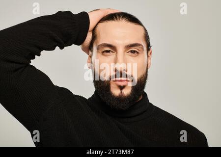 bellissimo uomo mediorientale con dolcevita nera, con sfondo grigio, ben vestito e curato Foto Stock