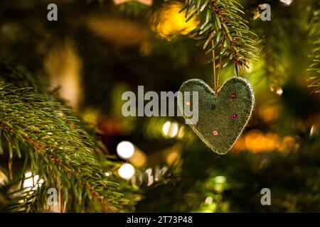 Un cuore in tessuto con decorazioni sull'albero di Natale in una luce suggestiva per Natale Foto Stock