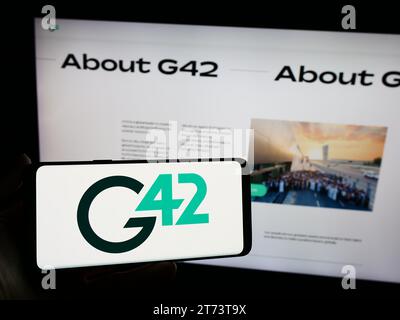 Persona che possiede uno smartphone con il logo della società tecnologica degli Emirati Group 42 Holding Ltd (G42) di fronte al sito web. Concentrarsi sul display del telefono. Foto Stock