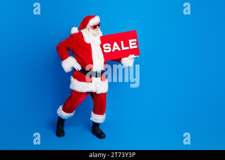 Foto integrale del poster di vendita dell'anziano uomo anziano vestito da elegante costume da babbo natale isolato su sfondo di colore blu Foto Stock