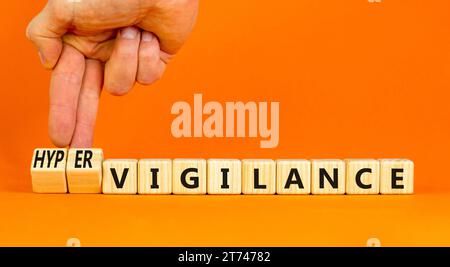 Simbolo di vigilanza o ipervigilanza. Parole concettuali Vigilance Hypervigilance su blocchi di legno. Splendido sfondo arancione. Mano psicologa. Psycholog Foto Stock