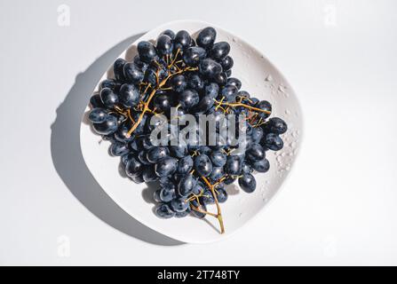 Grappoli di uva blu in un piatto bianco su sfondo bianco. Bacche, raccolta estiva, alimentazione sana Foto Stock