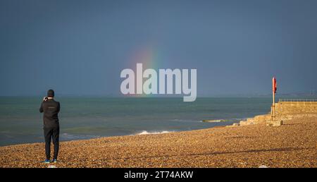 Qualcuno che scatta foto di un arcobaleno sul lungomare la mattina presto mentre la pioggia entra. Brighton, Sussex, Inghilterra, Regno Unito Foto Stock