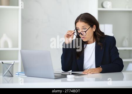 Una donna d'affari scioccata seduta in ufficio che guarda lo schermo del notebook Foto Stock