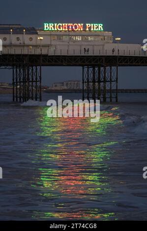 Vedute lontane del Palace Pier illuminato di notte da Brightons che si riflette sull'acqua, Brighton, Sussex, Inghilterra, Regno Unito Foto Stock