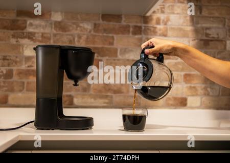 La mano di una donna versa il caffè da una caffettiera in una tazza in cucina. La vita familiare. Foto Stock