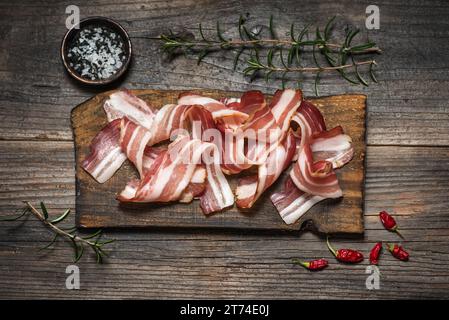 Pancetta affumicata arrotolata su un tagliere, con spezie diverse su fondo di legno Foto Stock