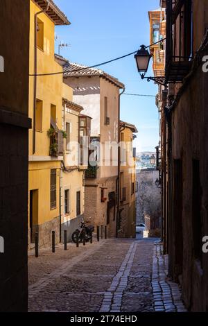 Stretta strada di ciottoli medievale spagnola con vecchie case residenziali, balconi tradizionali e lampade da strada in vecchio stile, motocicletta parcheggiata di fronte. Foto Stock