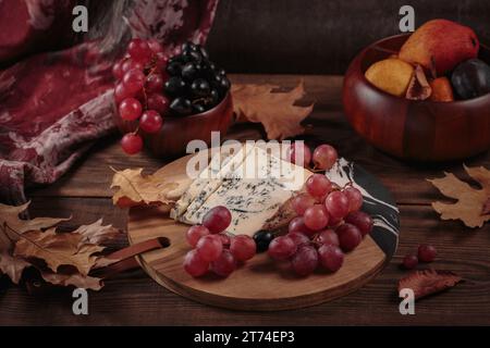 Piatto di formaggi servito con frutta autunnale e foglie secche Foto Stock