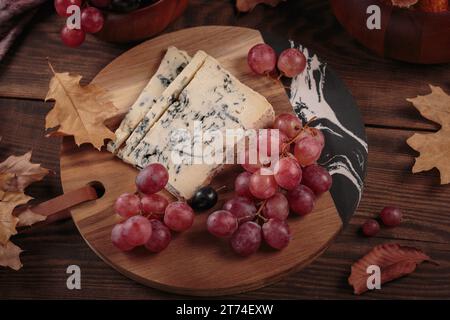 Piatto di formaggi servito con frutta autunnale e foglie secche Foto Stock