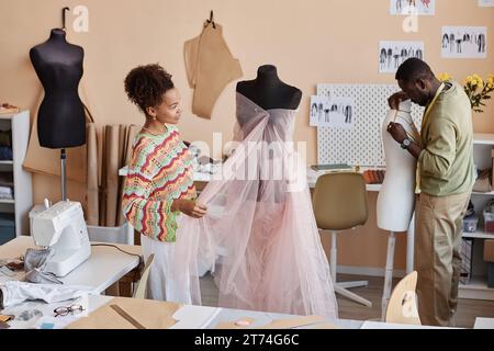 Due giovani colleghi stanno accanto ai manichini e creano nuovi vestiti da quelli vecchi mentre lavorano sulla collezione di moda stagionale Foto Stock