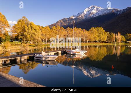Splendida vista autunnale sul lago con alberi in acqua a novembre, cascata sul lago di Como, Lombardia, Italia - cime montuose e barche attraccate Foto Stock