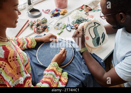 Primo piano di due designer afroamericani che creano eleganti ricami con fili e perline su tela e retro di una giacca in denim Foto Stock