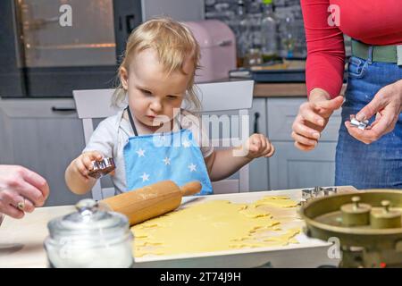 L'adorabile bambino taglia i biscotti dalla pasta nella cucina domestica. Orizzontalmente. Foto Stock