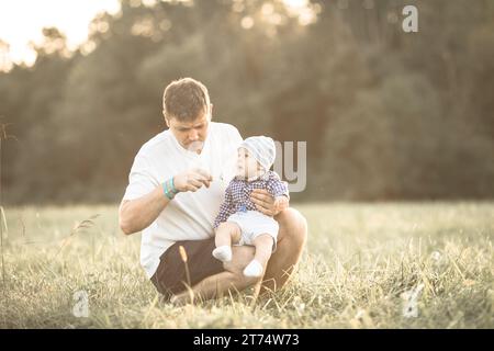 Un papà si diverte a divertirsi in un campo estivo, mentre il padre lancia un bambino. La famiglia allegra guarda con gioia e amore Foto Stock