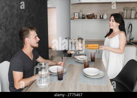 Giovane donna sorridente che serve mais al vapore la sua colazione di famiglia Foto Stock