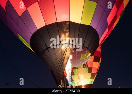 Mongolfiere che brillano di notte mentre il pilota accende il bruciatore per riempire l'involucro della mongolfiera con aria calda. Foto Stock