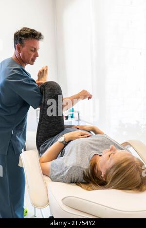 Fisioterapista che lavora alle gambe della donna per il benessere e il sostegno alla disabilità. Shot verticale Foto Stock