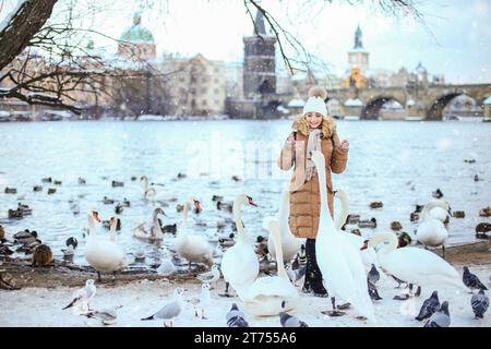 Ragazza che dà da mangiare ai cigni vicino al Ponte Carlo in inverno Foto Stock