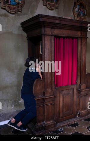 La donna confessa all'interno di una bella chiesa di San Carpoforo con luce solare a Bissone, Ticino, Svizzera Foto Stock