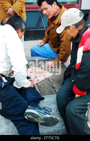 Un gruppo di amici discutono di strategia mentre giocano a Xiangqi, una forma di scacchi cinesi, in un parco cittadino Foto Stock