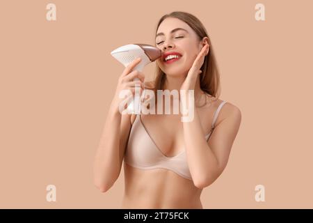 Bellissima giovane donna che depone il viso con un moderno fotoepilatore su sfondo marrone Foto Stock