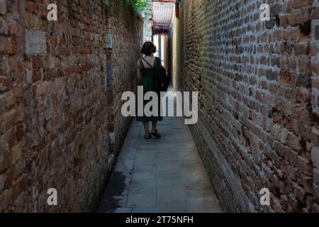 Dietro a una donna che cammina in uno stretto vicolo tra due edifici murati in mattoni Foto Stock