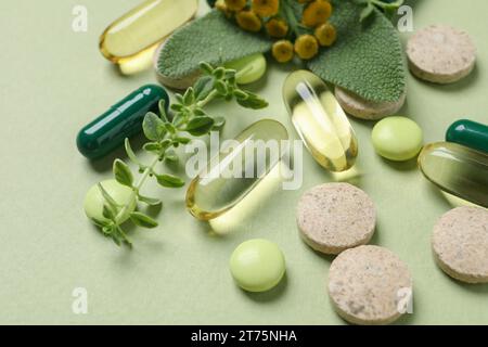 Pillole ed erbe diverse su sfondo verde chiaro, primo piano. Integratori alimentari Foto Stock