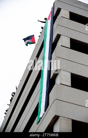 Austin, Texas, USA. 13 novembre 2023. I sostenitori palestinesi sventolano una grande bandiera palestinese mentre guardano migliaia marciare dal Campidoglio di Austin in Texas per protestare contro l'assedio e il bombardamento di Gaza da parte di Israele il 12 novembre. Il bombardamento indiscriminato ha ucciso undici mila civili ed è al suo secondo mese. (Immagine di credito: © Jaime Carrero/ZUMA Press Wire) SOLO USO EDITORIALE! Non per USO commerciale! Foto Stock