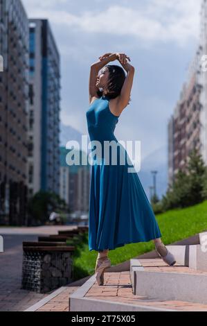 Bella ballerina asiatica in abito blu che posa sulle scale all'aperto. Paesaggio urbano. Foto Stock