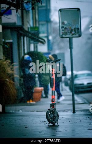 Una Vespa arancione parcheggiata sul marciapiede bagnato in città Foto Stock