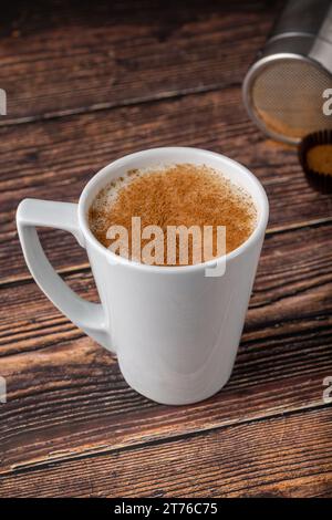 La cannella spruzzò il salep in una tazza bianca sul tavolo di legno Foto Stock