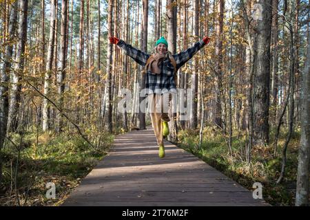Brilla di felicità corsa femminile, salto, volo su un sentiero di legno nella pineta in una giornata di sole Foto Stock