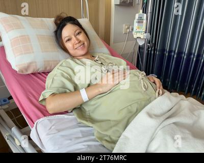 paziente donna incinta felice sta riposando su un letto in ospedale Foto Stock