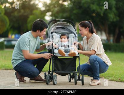 genitore felice (padre e madre) che parla e gioca con il bambino nel passeggino mentre riposa nel parco Foto Stock