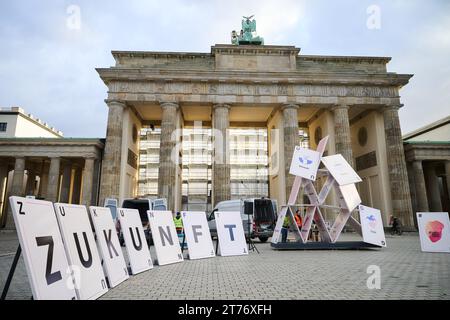 14 novembre 2023, Berlino: "Futuro" è scritto su carte da gioco di grandi dimensioni di fronte alla porta di Brandeburgo, mentre una casa di carte crollata con le parole "ambiente, denaro, istruzione, cibo, sicurezza..." sta per essere eretto dietro di esso. Diverse organizzazioni per l'assistenza ai bambini, tra cui Terre des hommes e Save the Children, vogliono utilizzare la campagna "Luft nach oben - keine Zeit für Kürzungen" (Air to the top - no time for cuts) per chiedere al governo tedesco di invertire i tagli ai finanziamenti allo sviluppo. Foto: Annette Riedl/dpa Foto Stock