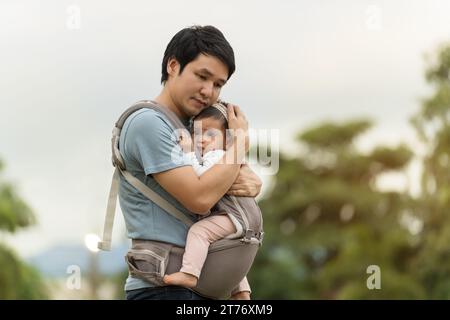 padre che consolava il suo bambino piangente in una portabicchieri nel parco Foto Stock