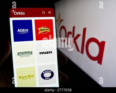 Persona che possiede un telefono cellulare con una pagina Web della società norvegese Orkla ASA davanti al logo aziendale. Concentrarsi sul centro del display del telefono. Foto Stock