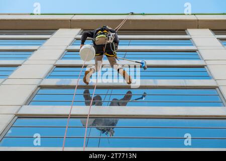 Guardando verso l'alto una lavavetri penzolante da una corda sul lato di un edificio a Melbourne, Victoria, Australia Foto Stock