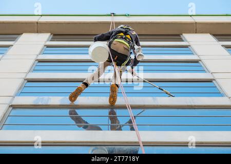 Guardando verso l'alto una lavavetri penzolante da una corda sul lato di un edificio a Melbourne, Victoria, Australia Foto Stock