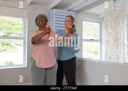 Fisioterapista femminile caucasica e paziente afrcia americana anziana con pesi, spazio copia Foto Stock