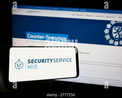 Persona in possesso di un cellulare con il logo dell'agenzia britannica di controspionaggio Security Service (MI5) davanti alla pagina web. Concentrarsi sul display del telefono. Foto Stock
