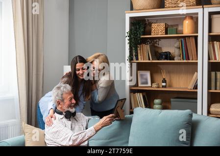 Riunione di famiglia. Padre, madre e figlia nella casa di famiglia, ricordano il passato guardando le vecchie foto della loro giovinezza. Nostalgia e ha Foto Stock