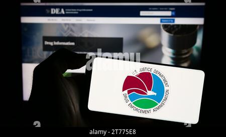 Persona in possesso di un telefono cellulare con il sigillo della United States Drug Enforcement Administration (DEA) davanti alla pagina Web. Concentrarsi sul display del telefono. Foto Stock