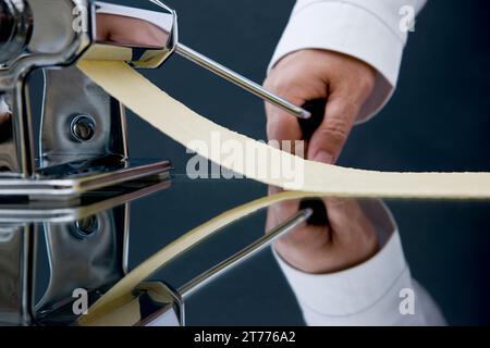 In prossimità di uno chef mano girando la maniglia di una pasta maker con pasta in uscita Foto Stock