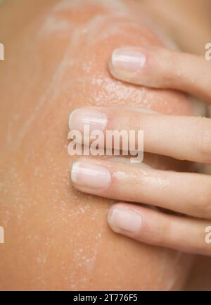 Extreme close up di una donna mano sfregamento del gel per la doccia sulla sua spalla Foto Stock